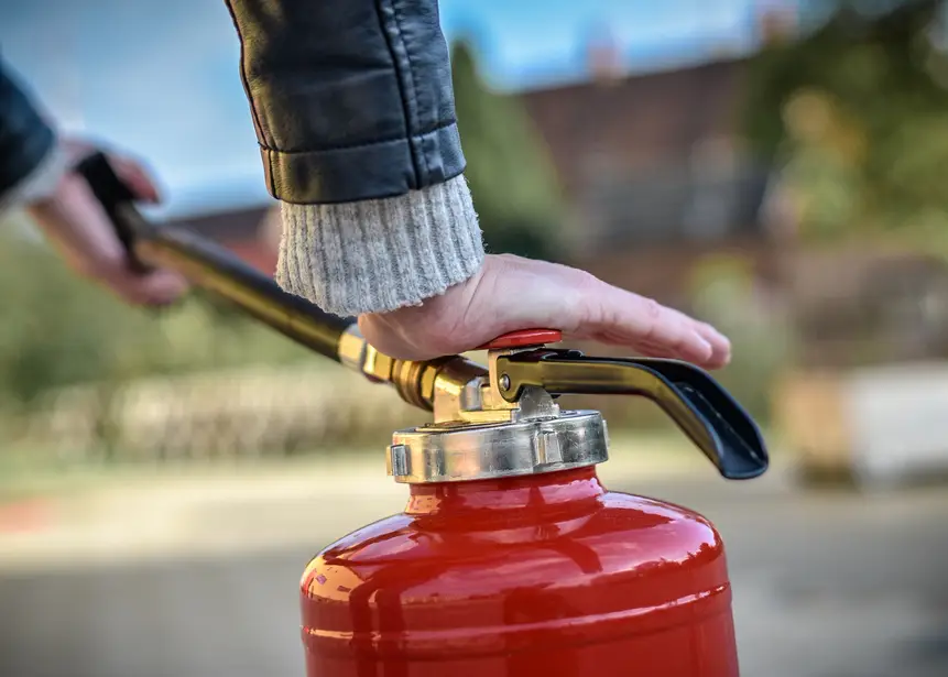 Hand prüft das Ventil eines roten Feuerlöschers bei der Wartung