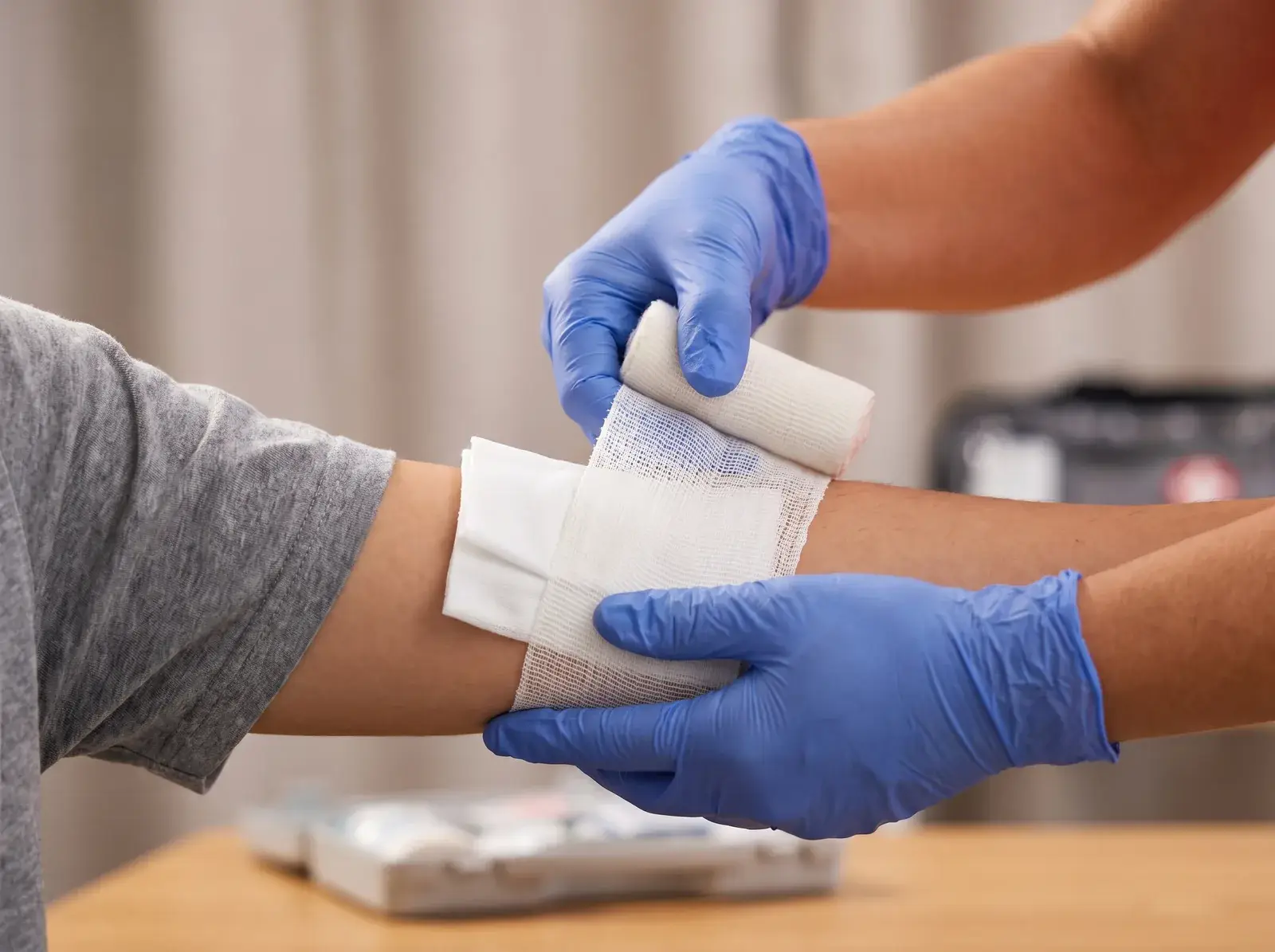 Behandschuhte Hände versorgen eine Verletzung am Unterarm mit einem Druckverband