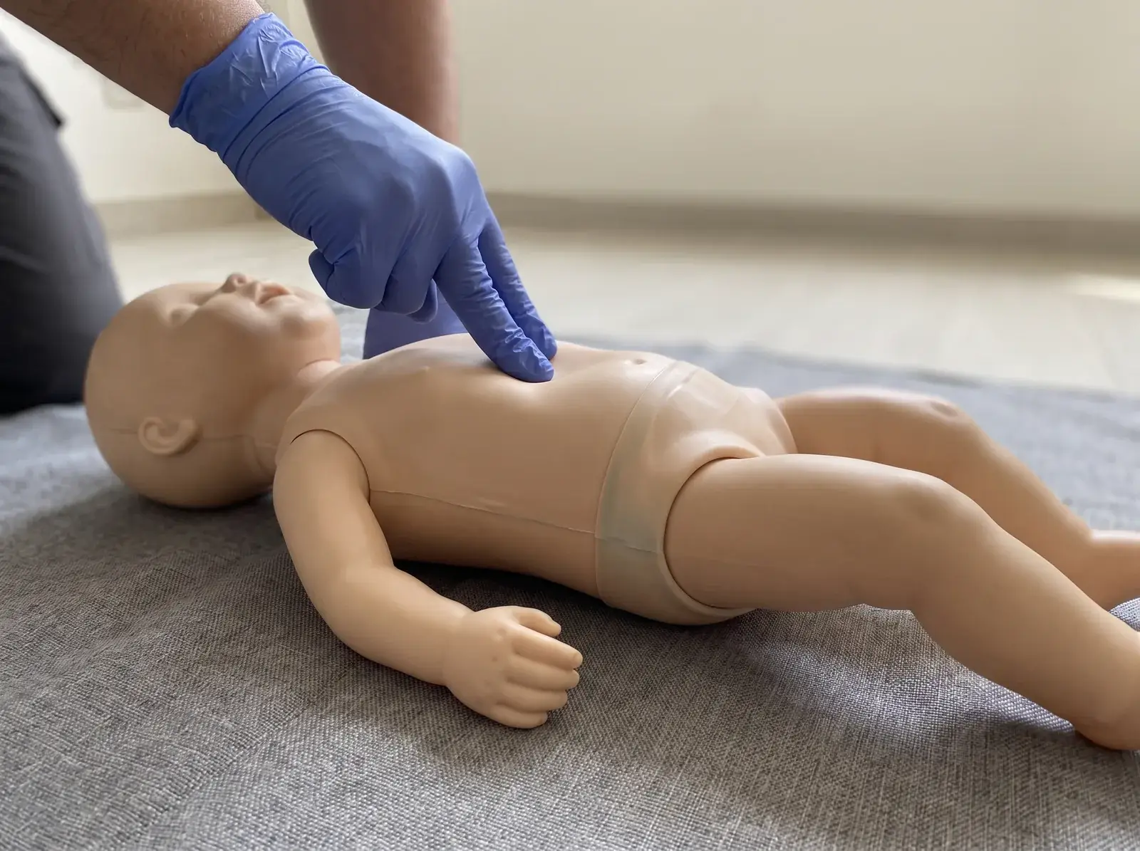Zwei Finger drücken auf den Brustkorb einer Säuglings-Übungspuppe bei der Kinderreanimation
